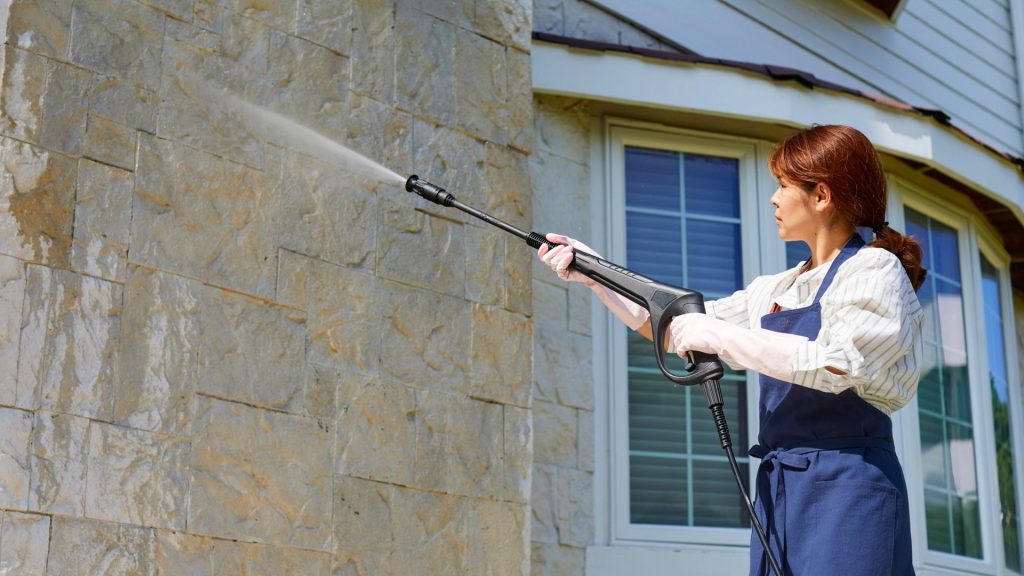 Woman Using Pressure Washer on Stone Wall